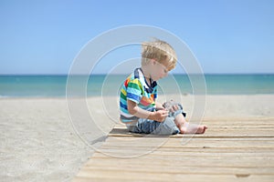 Boy sitting on a wooden walkway on the beach