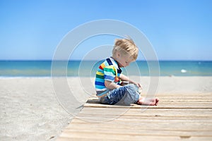 Boy sitting on a wooden walkway on the beach