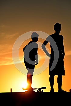 Boy with skateboard and friend on summer sunset