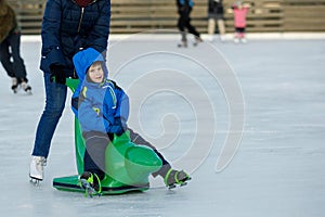 The boy is skating at the rink. The child learns with his parent to ice skate