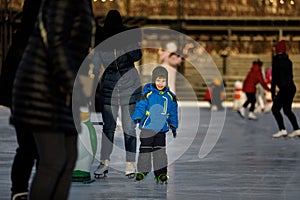 The boy is skating at the rink. The child learns with his parent to ice skate