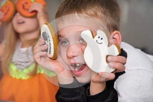 A boy in skeleton costume and pumpkin girl eat gingerbread cookies for Halloween