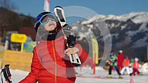 Boy at a ski resort. A child in full equipment for skiing, in a red jacket, glasses and a helmet looks at the sky. The