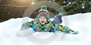 Boy sledding in a snowy forest. Outdoor winter fun for Christmas vacation.