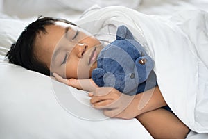 Boy sleeping on bed with teddy bear white pillow and sheets