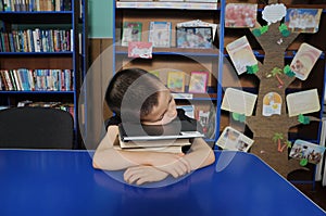 Boy sleeping in library exausted, putting head on pile of book photo