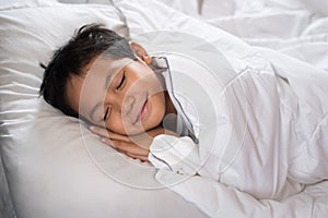 Boy sleeping with smile face on white bed sheet and pillow