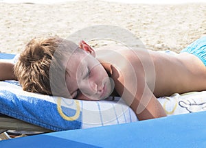A boy sleeps on the beach under strong sunlight. Danger of sunstroke or burn. The risk of overheating and dehydration photo