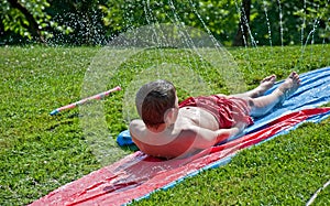 Boy Sliding on Plastic in Summer Sprinkler