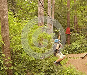 Boy on a sliding swing. Child in forest adventure park. Kids climb on high rope trail. Kid in a blue helmet on a sliding