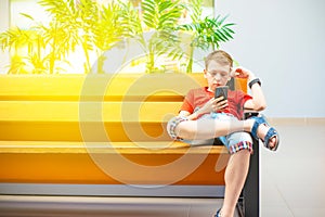 A boy with a smartphone sits on a bench and writes and reads a message. Photo with tinting