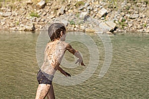 A boy smeared with river mud plays on the background of a mountain river