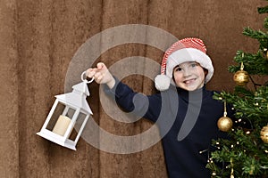 The boy smiles, with a fallen tooth, peeking out from the charged Christmas tree, with a lantern in hand.