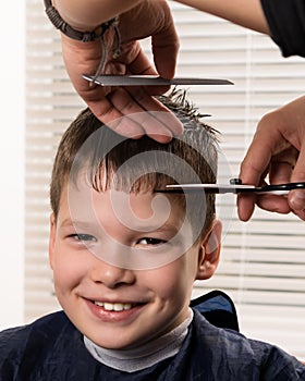 The boy smiles during the haircutting process by the hairdresser