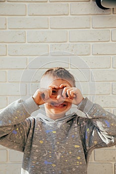 The boy smiles and shows a heart with his fingers. Portrait of a child against a white brick wall