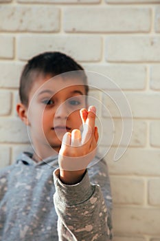 The boy smiles and shows a heart with his fingers. Portrait of a child against a white brick wall