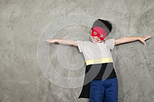 The boy smiling dressed up in superhero costume, he pretends to open arms in the studio for the educational.