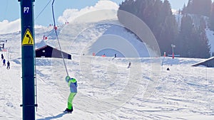 Boy on snowboard go up holding t-bar ski lift at alpine resort