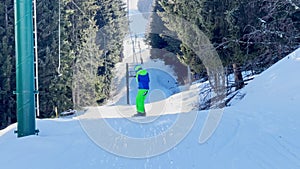 Boy on snowboard go up holding t-bar ski lift at skiing resort