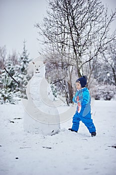 boy and snowman, happy beautiful child building snowman in garden, winter happy time, kid on snow