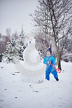 boy and snowman, happy beautiful child building snowman in garden, winter happy time, kid on snow