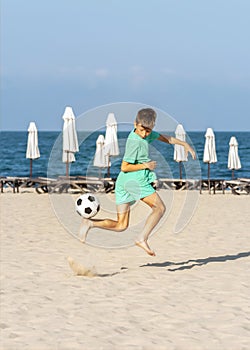 Boy soccer player enjoying game of beach football on sand, juggling ball with his bare feet. Summer holidays