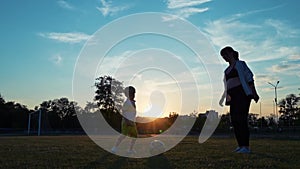 Boy soccer player playing with his pregnant mother with a ball in the stadium, against the backdrop of the sunset