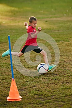 Boy soccer player in red sport uniform training kicking ball, prepare to match on football field in motion. Playing