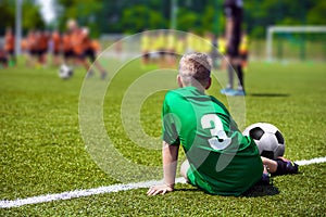 Boy soccer player on sports field. Child sitting on football grass field