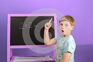 The boy solves the math equation 2 + 2 written on the blackboard. The child holds his finger up
