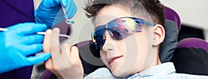 A boy in special glasses in the dentist`s chair. he curiously studies medical instruments in the hands of a doctor