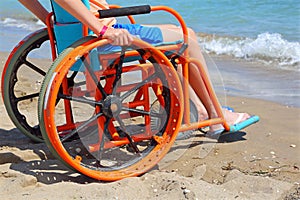 Boy on a special wheels chair observes the sea from the beach