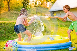 Boy splashing girl with water gun, garden swimming pool