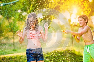 Boy splashing girl with water gun, sunny summer garden