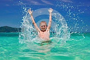 Boy splashing water in sea. Playful child 10 years old surrounded by colorful nature. Bright blue sky and shimmering sea.