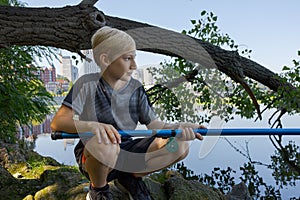 A boy squats on rocks and catches fish. Sport fishing on the river in summer