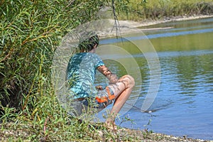 Boy Squatting Behind Bushes and Fishing in Lake