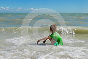 Boy squatting in the ocean, looking at the horizon