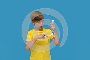 Boy squeezes toothpaste on the brush isolated on blu background.