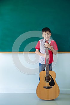 Boy stading with guitar in front of blackboard