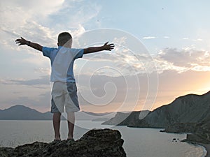 Boy stand on mountain top with hands up