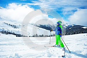 Boy stand on ski track in sport outfit observing the mountain