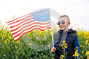 Boy standing with the american flag on the green and yellow field celebrating national independence day. 4th of July concept