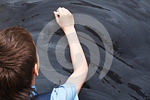 Boy standing back in front of school blackboard and writing