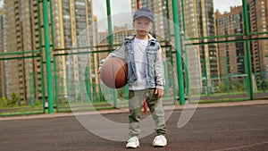 Boy is standing on basketball court holding ball in residental district in city.