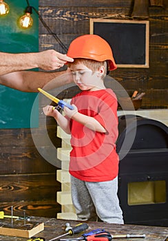 Boy standing behind the table with various tools. Daddy taking care about sons safety. Male hands holding orange