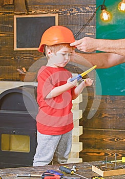Boy standing behind the table with various tools. Daddy taking care about sons safety. Male hands holding orange