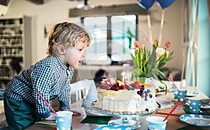 A boy standing on a chair, blowing out candles on a birthday cake.