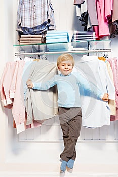 Boy standing among clothes on hangers and shelf
