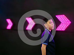 Boy Standing by Dark Wall with Illuminated Vibrant Pink Arrows